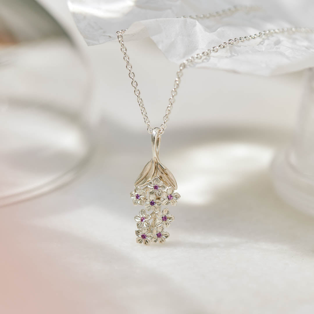 Forget-Me-Not flower inspired pendant with leaf detail, manufactured in sterling silver, set with lilac sapphires, and on a sterling silver rolo chain