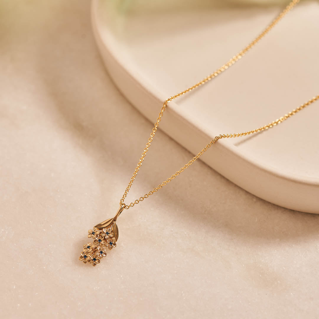 Forget-Me-Not flower inspired pendant with leaf detail, manufactured in 9ct yellow gold, set with light blue sapphires, and on a 9ct yellow gold rolo chain