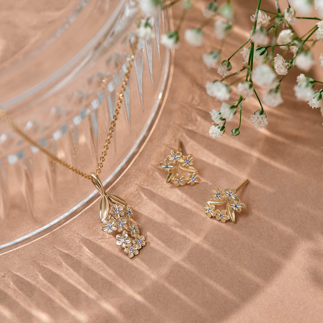 Forget-Me-Not flower inspired pendant with leaf detail, manufactured in 9ct yellow gold, set with light blue sapphires, and on a 9ct yellow gold rolo chain. Photographed with the Sapphire Forget-Me-Not studs