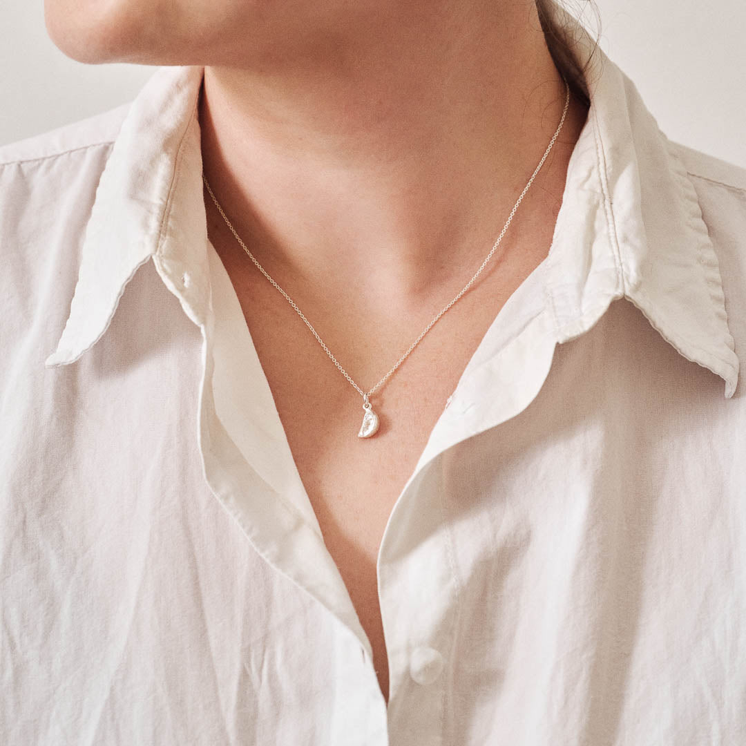 A miniature silver citrus wedge jewellery charm on a silver rolo chain. Photographed being worn.