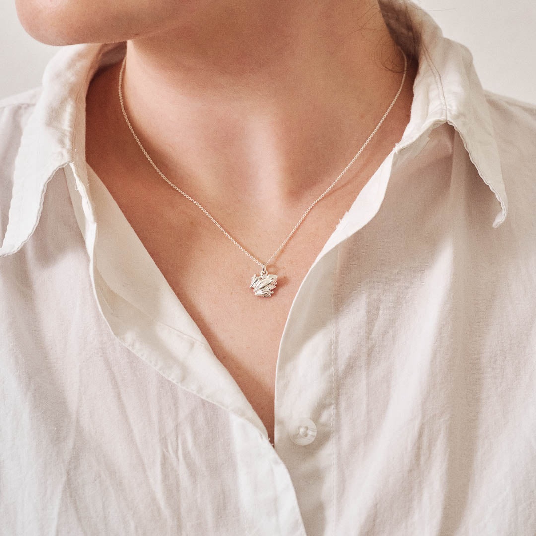 A miniature silver frog jewellery charm on a silver rolo chain. Photographed being worn.