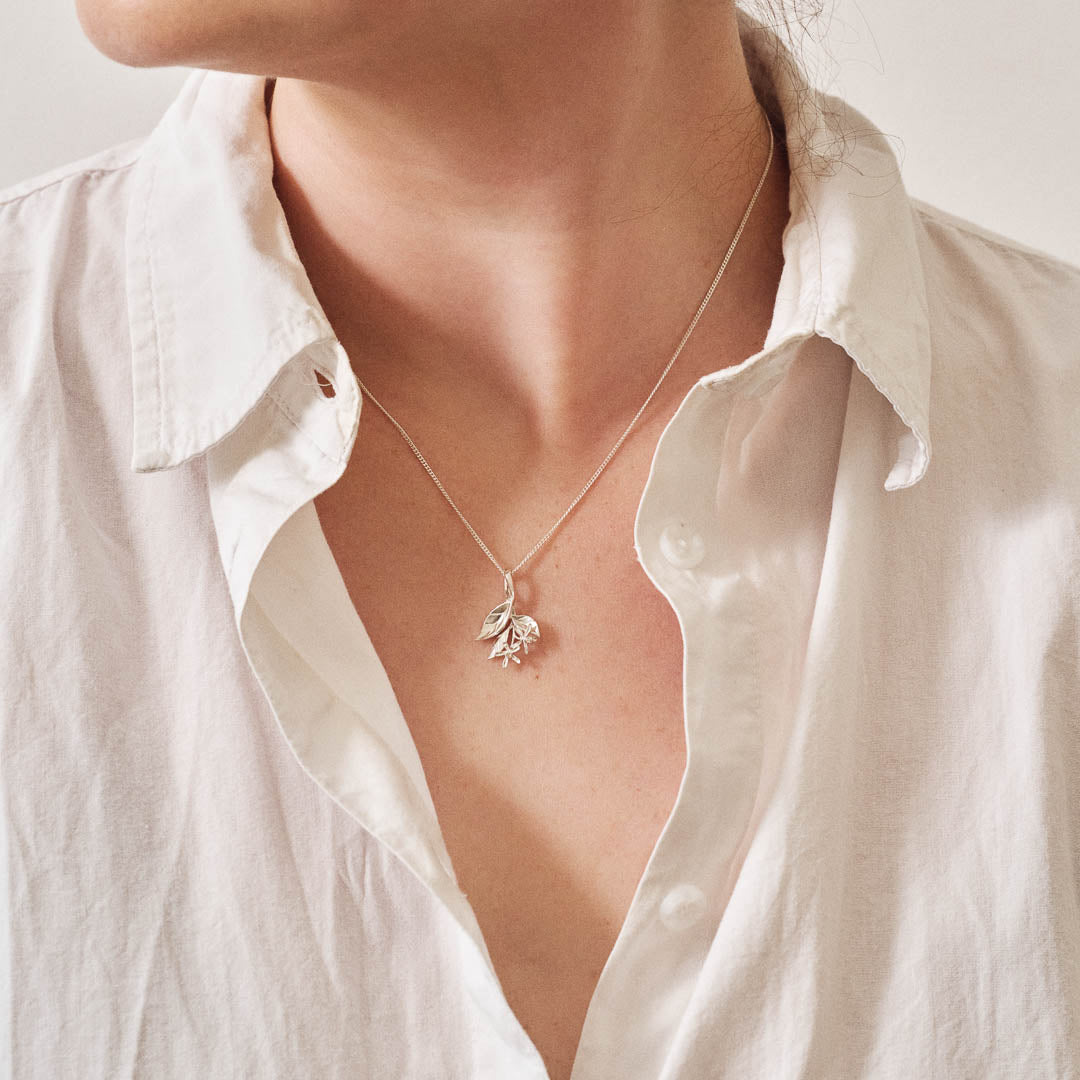 A silver pendant featuring leaves and lemon blossom flowers on a silver curb chain being worn.