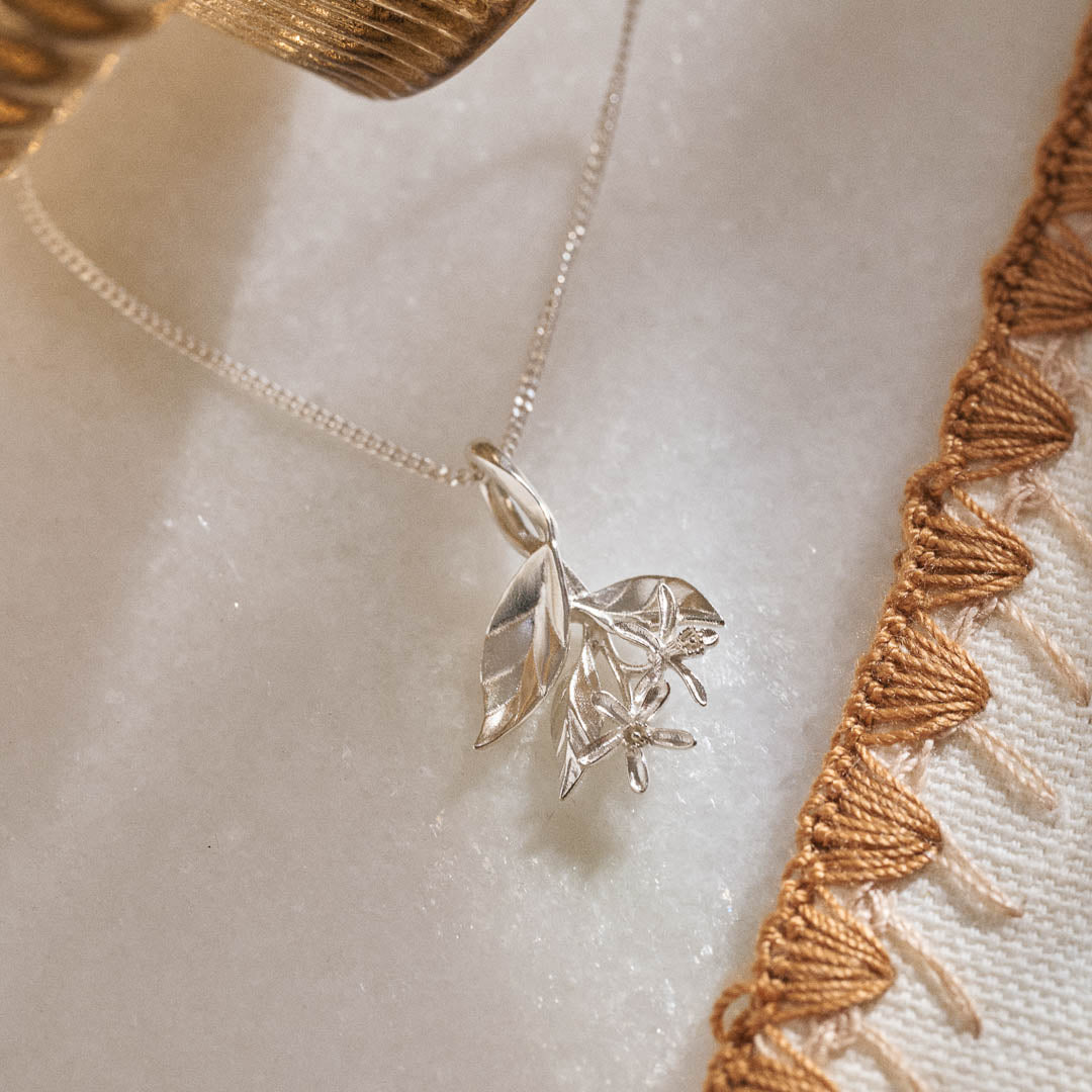A silver pendant featuring leaves and lemon blossom flowers on a silver curb chain.