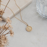 Yellow gold disc pendant with wreath border and an engraved initial.