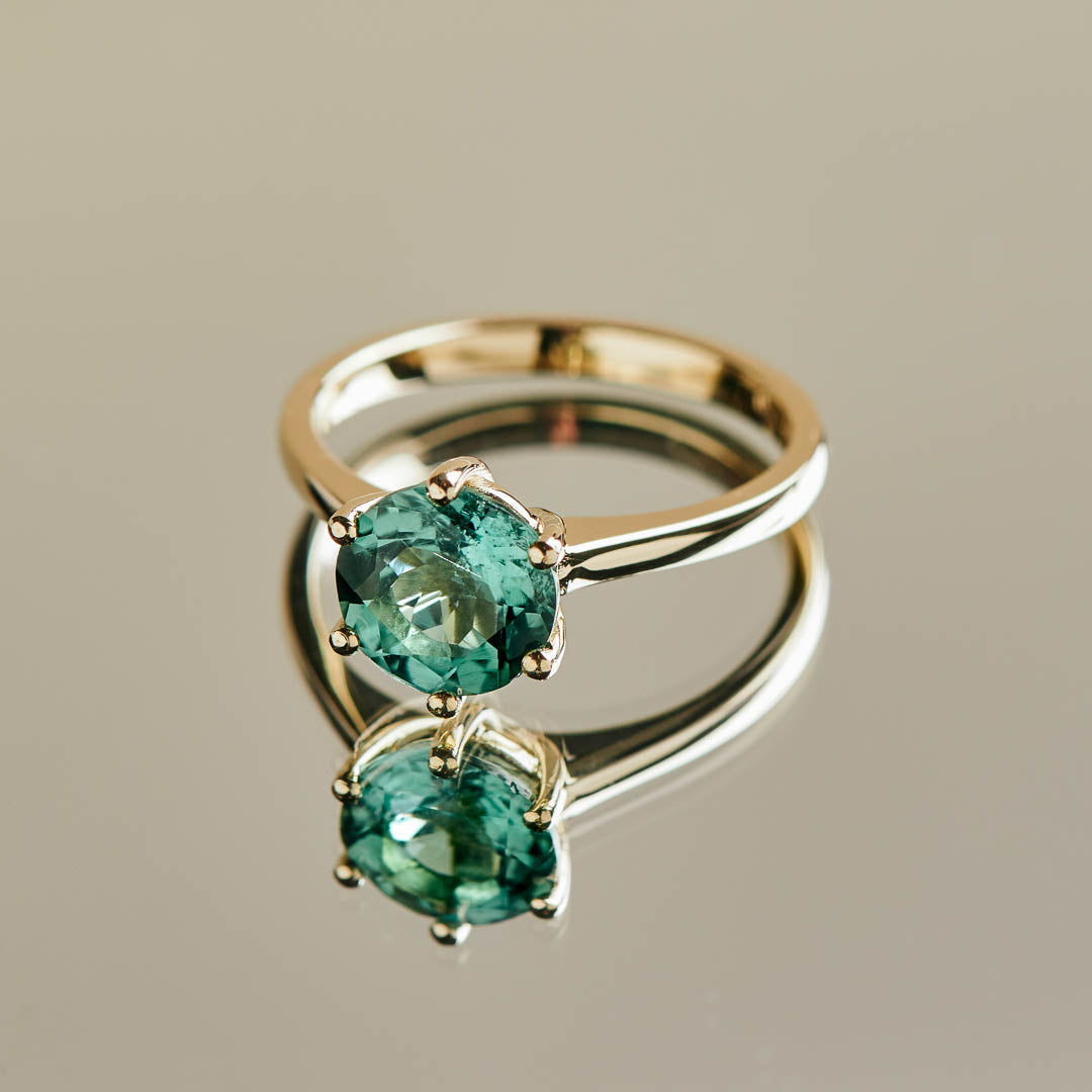 A bright and striking blue round tourmaline set in a classic six claw yellow gold ring