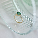 A bright and striking blue round tourmaline set in a classic six claw yellow gold ring