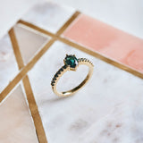 A vibrant blue green Tourmaline set in a classic six claw setting, accentuated with black diamonds set into the yellow gold band