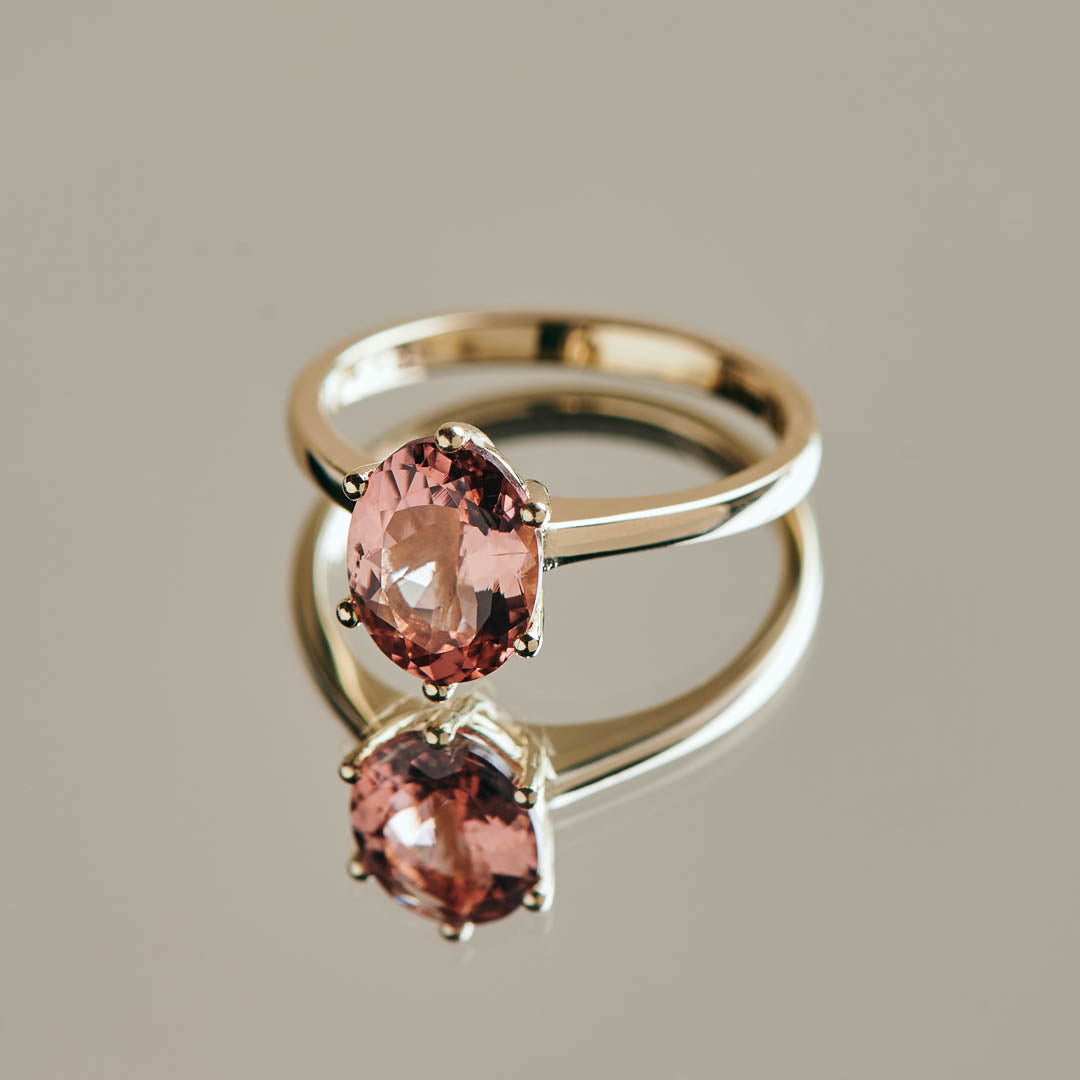 A blush pink oval tourmaline set in a classic six claw yellow gold ring