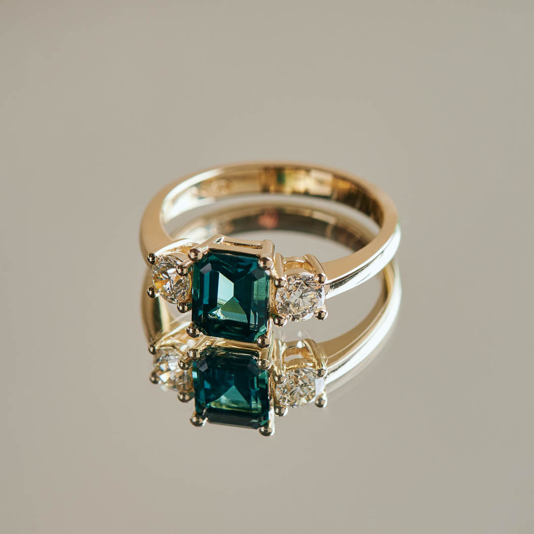 A striking blue emerald cut tourmaline flanked by two natural beautiful diamonds