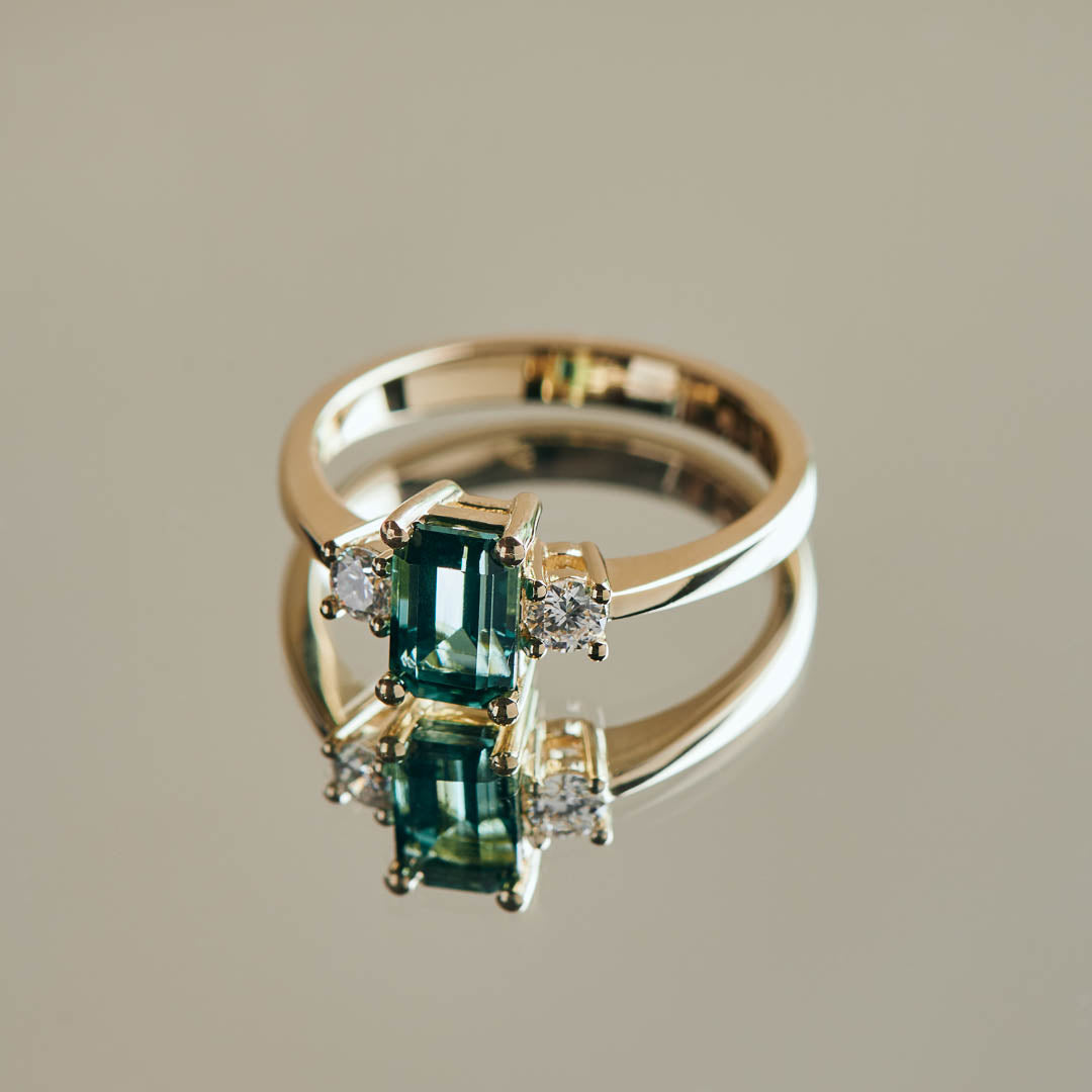 A beautiful teal tourmaline that reminded us of the ocean flanked by two natural diamonds set in a design that is classic and timeless