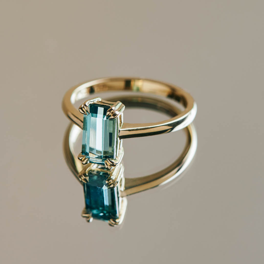 An emerald cut teal tourmaline set in a 9ct yellow gold ring with double cat claws