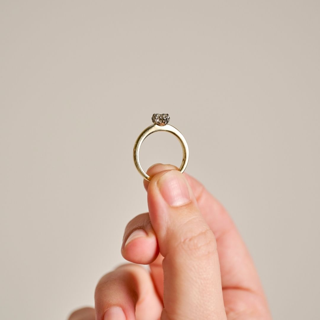 A close-up of a hand holding the two-tone Botanica Protea Ring to show the rings delicate proportions and considered details. Photographed against a plan grey background.