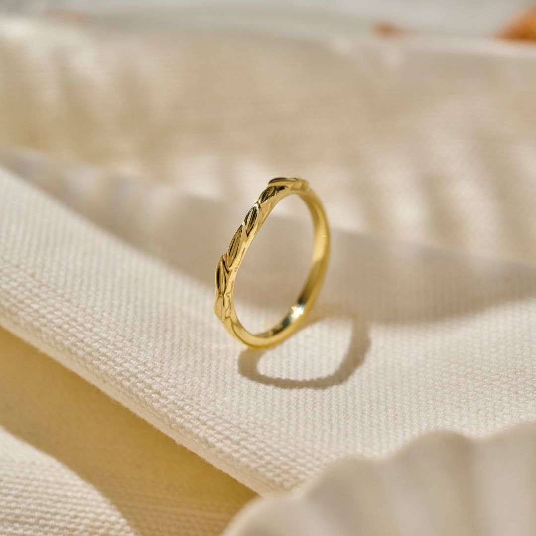 An organic 9ct Yellow gold wedding ring with a polished curved overlapping leaf design, resting on a soft, cream-coloured woven  fabric.