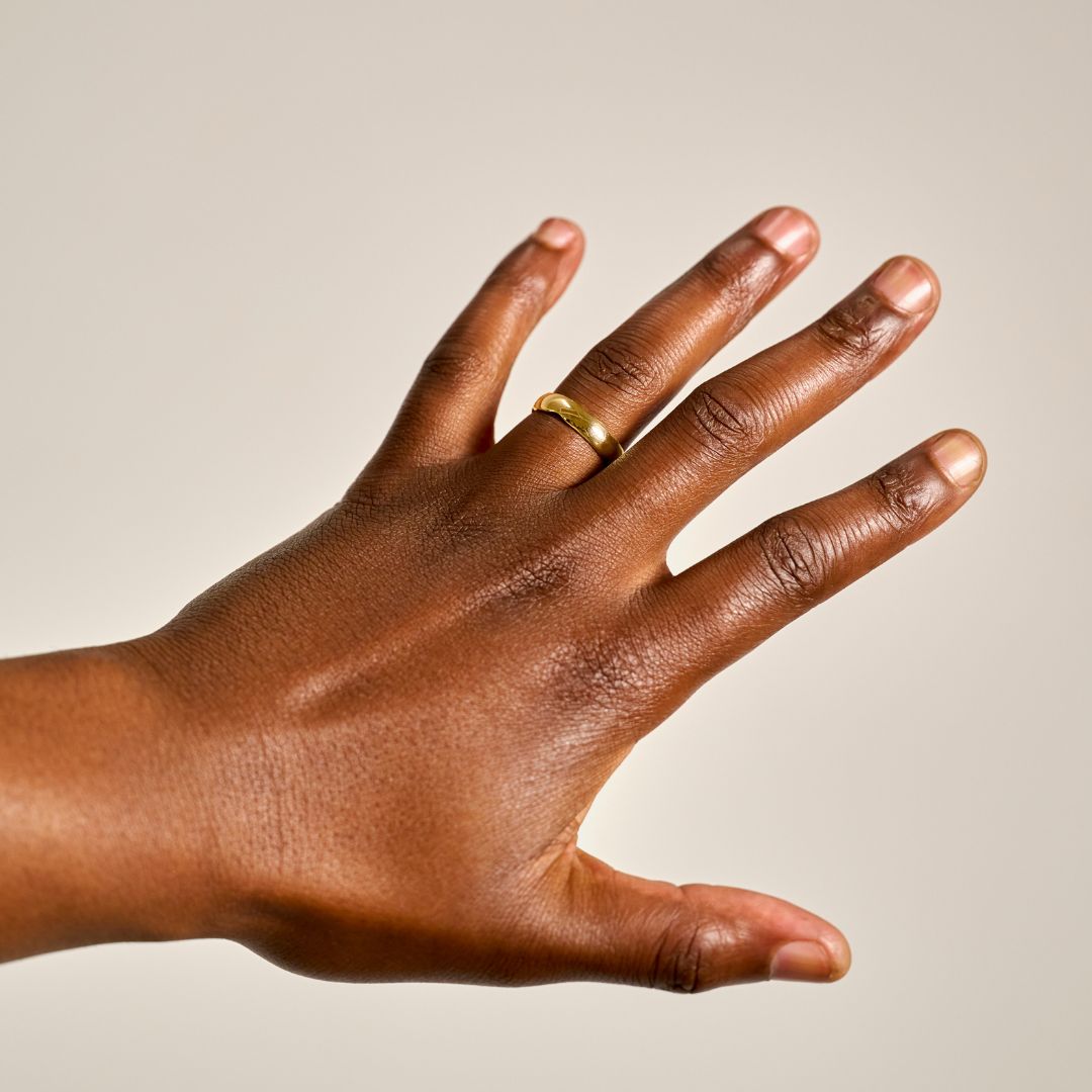 A close-up of a man's hand wearing a unique organic gold wedding ring, set against a plain light beige background.