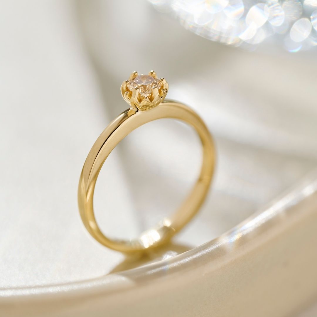 A solid yellow gold Botanica Protea Ring, photographed from the side view to show the solid Protea petal detail and rounded shank. The Protea Ring is photographed on a cream ceramic base. 