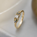 Yellow gold cluster ring set with a central natural diamond and additional blue, green, and yellow sapphires on either side. on a neutral background