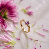 Yellow gold ring set with a purple sapphire and natural diamonds, featuring lavender-inspired hand engraving on the shank with natural diamonds on pink flowers